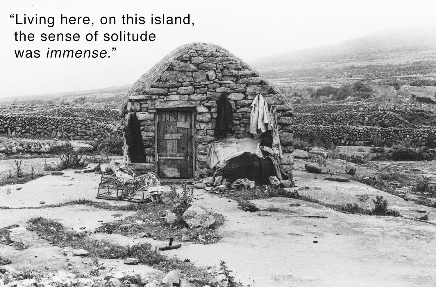 Grayscale photo of a stone hut inscribed with 'Living here, on this island, the sense of solitude is immense.'