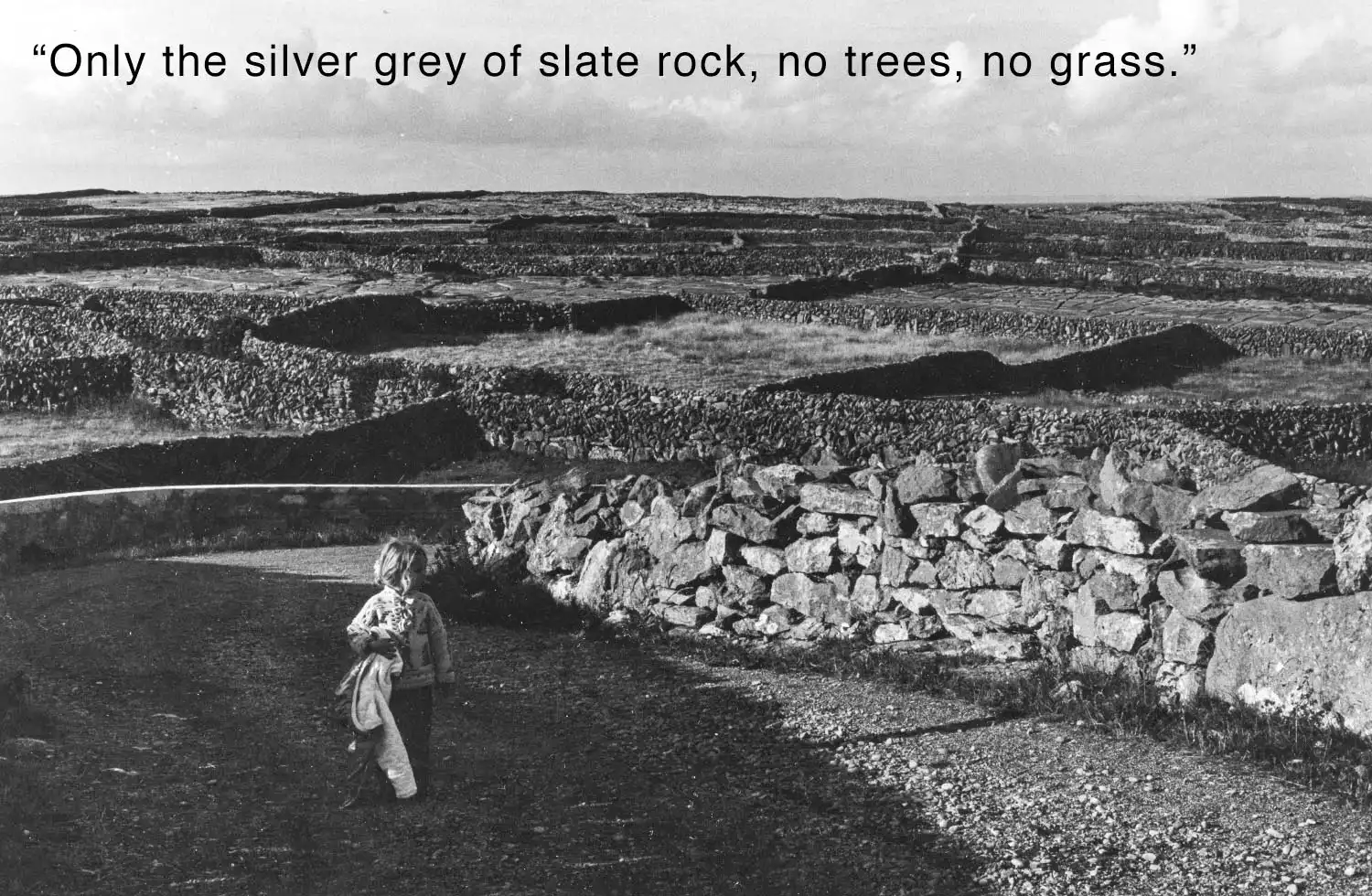 Grayscale landscape of a stone walls with a child in the foreground inscribed with 'Only the silver grey of slate rock, no trees, no grass.'