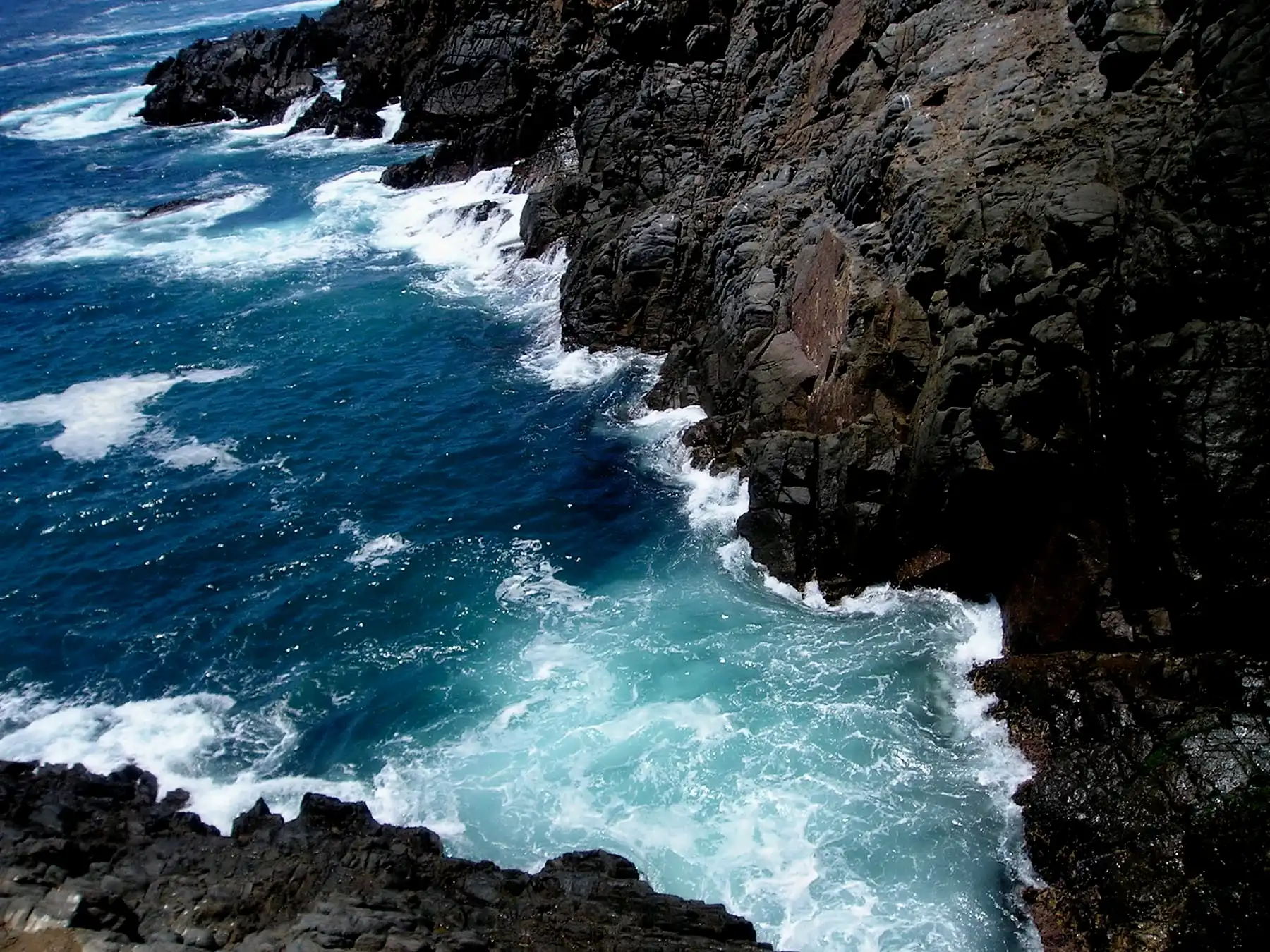 Waves splashing against black cliffs viewed from above